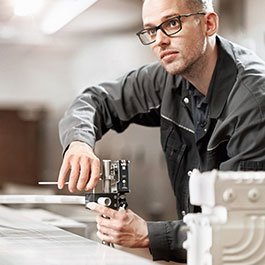 Ein Mann in Arbeitskleidung misst präzise mit einem Messgerät an einem Tisch in einer modernen Werkstatt.