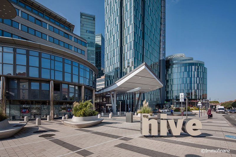 Vienna location: A clear blue sky above an elegant office building with glass fronts and the word 'hive' in the foreground.