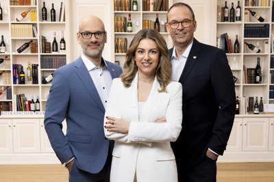 Management Rotkäppchen Mumm: Three people are standing smiling on a staircase, the woman in a white suit, the men in formal attire.