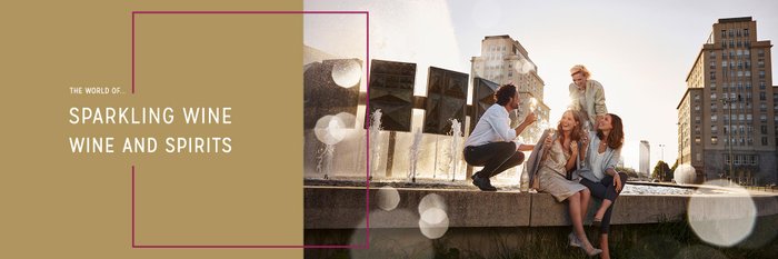 Four people celebrate happily with glasses in their hands, surrounded by water fountains.