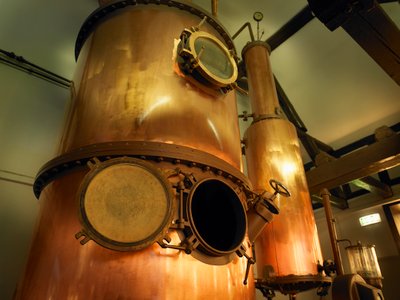 Die kupfernen Destillationsanlagen stehen majestätisch in einem Raum mit gedämpftem Licht und rustikalem Holzdekor.