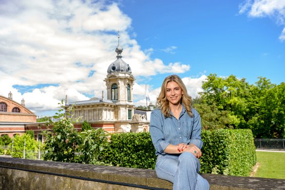 Porträtfoto Silvia Wiesner: Im Jeansanzug auf einer Mauer sitzend, im Hintergrund die Rotkäppchen Sektkellerei