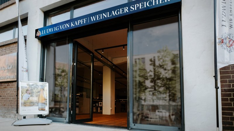 Die Fassade eines Weinlagers mit dem Namen 'Ludwig von Kapff' und einem Werbeschild, das ein Weinangebot bewirbt.