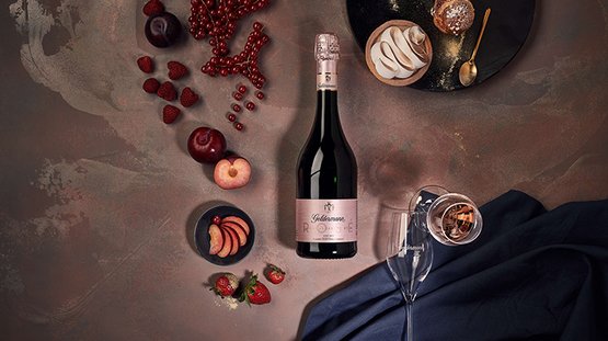 Ein eleganter Tisch mit einer Flasche Rosé-Sekt, frischen Früchten und einem Dessert auf einem dunklen Hintergrund.