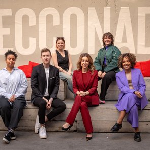 Eine Gruppe von sechs Personen, darunter CEO Silvia Wiesner, sitzt auf einer Holzbank vor einer Wand mit dem Schriftzug "SECCONADE". Rote Kissen im Hintergrund.