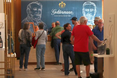 Zahlreiche Besucher stehen in einem eleganten Raum, einige halten Gläser, während sie an einem Empfangstresen stehen.