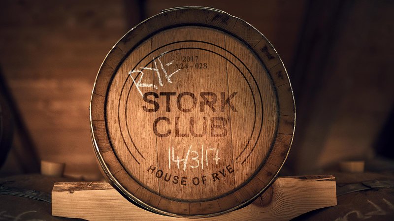 Ein Holzfass mit der Aufschrift 'STORK CLUB' und dem Datum 14/3/17 steht auf einem Holzständer in einem dunklen Raum.