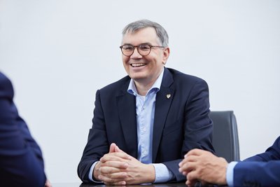 Christof Queisser in einem Anzug sitzt an einem Tisch und wirkt freundlich und offen während eines Gesprächs.