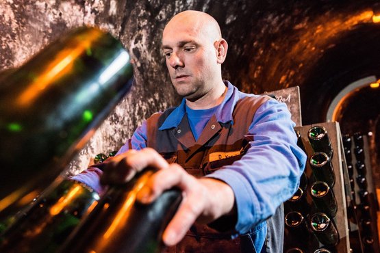 In a cool cellar environment, a man tends to bottles, his hands precise and purposeful at work.