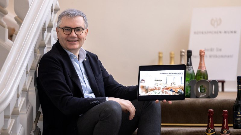 Ein lächelnder Mann sitzt auf einer Treppe und hält ein Tablet mit einer Präsentation über Genusskultur in der Gastronomie.