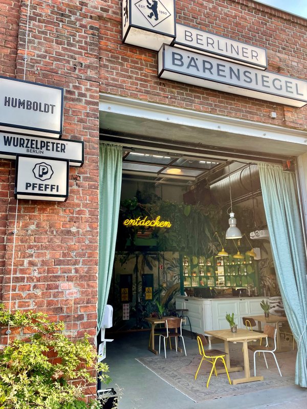 Außenfassade Bärensiegel: Ein einladender Eingangsbereich mit grünen Vorhängen, der einen Blick auf eine stilvolle Bar und gemütliche Sitzgelegenheiten bietet.