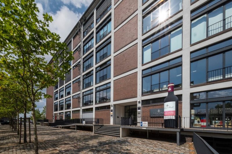 Standort Bremen: Ein modernes Gebäude mit großen Fenstern und einer auffälligen Weinflasche an der Fassade, umgeben von Bäumen.