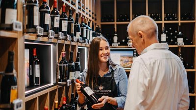 In einem eleganten Weinladen hält eine Frau eine Flasche Wein in der Hand und erklärt sie einem interessierten Mann.