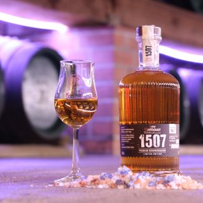 Eine Whiskyflasche und ein Glas auf einem Tisch mit Salzsteinen, im Hintergrund Fässer.