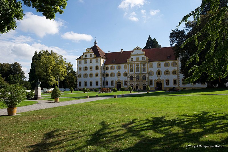 Standort Salem: Ein prächtiges Schloss mit gelben und weißen Fassaden, umgeben von gepflegten Gärten und Bäumen unter einem blauen Himmel.
