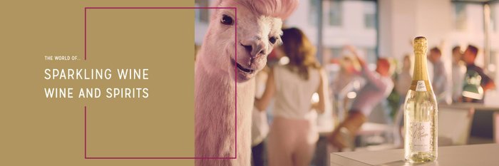A llama with a pink mane stands in a modern room with people in the background.