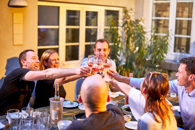 Freunde feiern zusammen, während sie an einem Tisch im Freien sitzen und auf den Abend mit Rosé anstoßen.