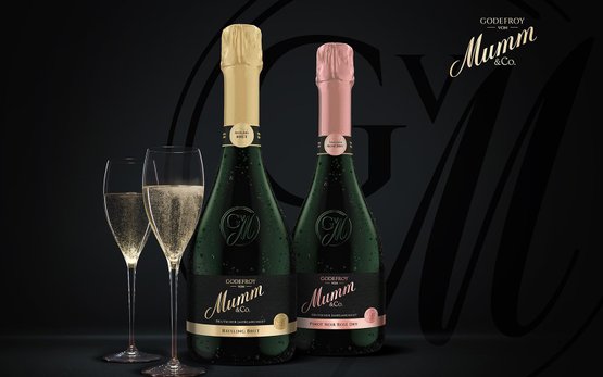 Zwei elegante Gläser mit sprudelndem Sekt stehen neben Flaschen von Mumm, die in einem stilvollen, dunklen Setting präsentiert werden.