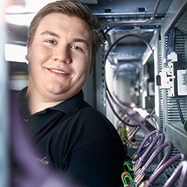 Ein junger Techniker lächelt, während er in einem Serverraum mit bunten Kabeln arbeitet, umgeben von moderner Technik.