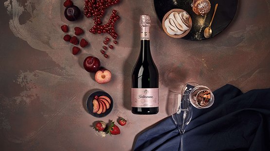 Ein eleganter Tisch mit einer Flasche Rosé-Sekt, frischen Früchten und einem Dessert auf einem dunklen Hintergrund.