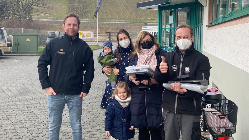 Eine Gruppe von fünf Personen steht lächelnd vor einem Gebäude, während sie verschiedene Gegenstände in den Händen halten.