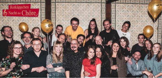 Die Teilnehmer der 'Nacht der Chöre' lächeln und feiern, während sie Getränke in der Hand halten und eine lebhafte Atmosphäre genießen.