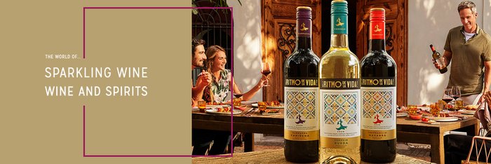 Three bottles of wine stand on a wooden table while a group of people happily celebrate together.