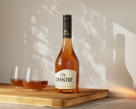 Eine Flasche Chantré Weinbrand steht auf einem Holzbrett, umgeben von zwei Gläsern mit goldenem Getränk.