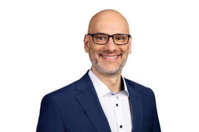 Markus Jauch: The man with a friendly smile has a grey beard and wears glasses while looking into the camera.