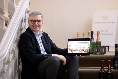 Ein lächelnder Mann sitzt auf einer Treppe und hält ein Tablet mit einer Präsentation über Genusskultur in der Hand.