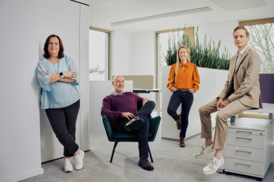 In a stylish office there are two women and two men, dressed in fashionable clothes and appearing friendly.