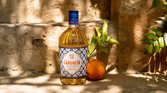 Eine Flasche Canonita aus Mallorca steht auf einer steinernen Oberfläche, umgeben von frischen grünen Blättern und einer Orange.