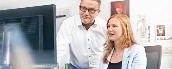Ein Mann und eine Frau schauen gemeinsam auf einen Computerbildschirm, während sie in einem modernen Büro arbeiten.