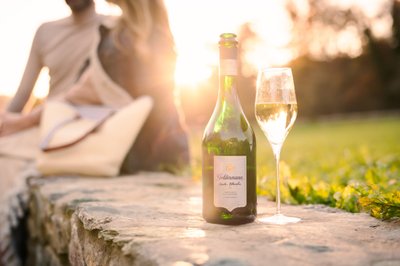 Geldermann: A green bottle of champagne stands on a stone, next to it a glass of sparkling champagne, while the sun sets.