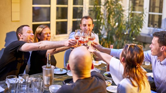 Friends celebrate together while sitting at an outdoor table and toasting the evening with rosé.
