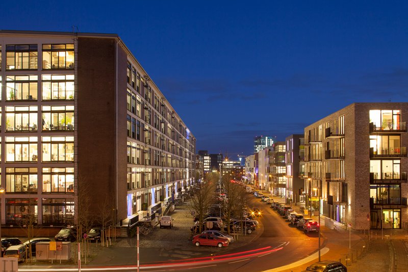 Standort Bremen: Eine moderne Stadtansicht bei Nacht, mit beleuchteten Bürogebäuden und einer lebhaften Straße voller Autos.
