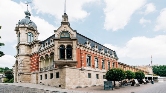 Freyburg: Ein historisches Gebäude mit einer beeindruckenden Fassade aus rotem Ziegel und Stein, umgeben von Bäumen und einem gepflasterten Weg.