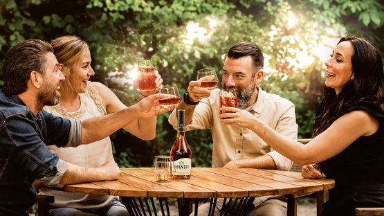 Three people clink glasses while a bottle of CHANTRÉ sits on the table, surrounded by a beautiful natural backdrop.