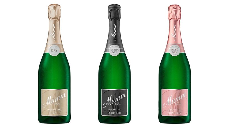 Drei Flaschen Sekt von Mumm stehen nebeneinander, jede mit einem einzigartigen Etikett: Dry, Extra Dry und Rosé Dry.