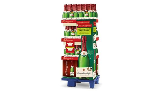 Ein stabiler Verkaufsständer mit Flaschen Sekt, dekoriert mit bunten Etiketten und einer auffälligen grünen Flasche in der Mitte.