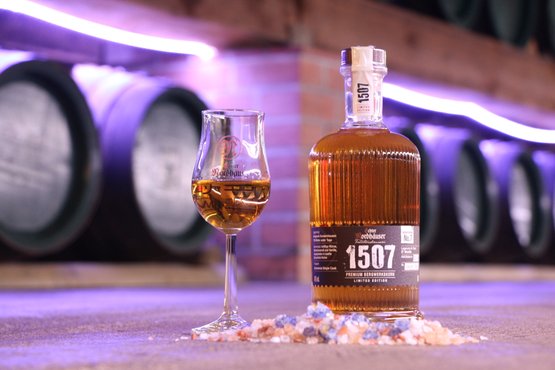 Eine Whiskyflasche und ein Glas auf einem Tisch mit Salzsteinen, im Hintergrund Fässer.