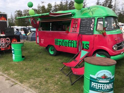 Ein farbenfroher Foodtruck mit der Aufschrift 'Pfeffi' bietet frische Getränke an, umgeben von grünen Stühlen und einer entspannten Atmosphäre.