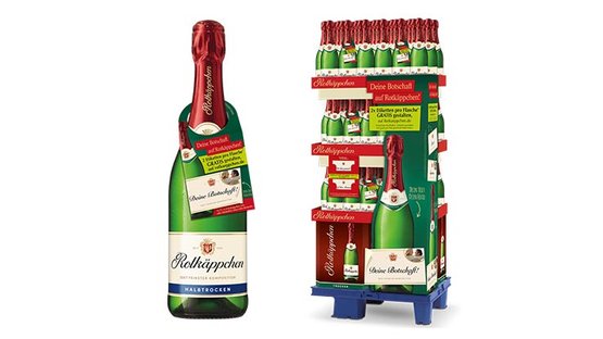Sag es mit Rotkäppchen: Eine Flasche Rotkäppchen Sekt steht neben einem Verkaufsdisplay mit mehreren Flaschen, das festlich dekoriert ist.