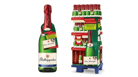 Sag es mit Rotkäppchen: Eine Flasche Rotkäppchen Sekt steht neben einem Verkaufsdisplay mit mehreren Flaschen, das festlich dekoriert ist.