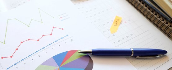 Auf einem Tisch liegen Diagramme und ein Kalender, während ein blauer Stift bereit zum Schreiben ist.