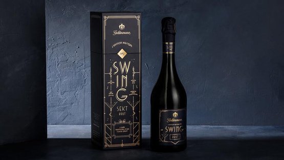 Eine elegante Flasche Sekt steht neben einer stilvollen Verpackung auf einem dunklen Hintergrund.