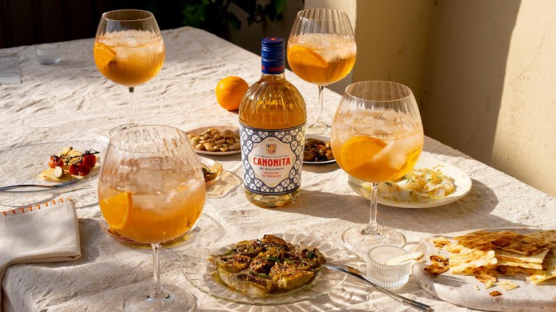 Ein Tisch gedeckt mit Gläsern voller orangefarbener Getränke, umgeben von verschiedenen Snacks und einer Flasche Canonita.