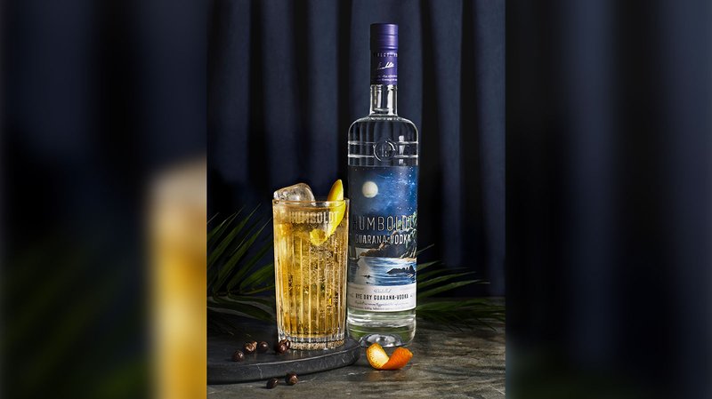 Ein Glas mit einem erfrischenden Getränk, garniert mit einer Limettenscheibe, steht neben einer Flasche Humboldt-Wodka.