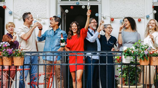 A joyful celebration on a balcony where people in festive attire toast with Rotkäppchen champagne and enjoy the blooming surroundings.