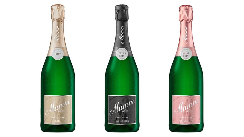 Drei Flaschen Sekt von Mumm stehen nebeneinander, jede mit einem einzigartigen Etikett: Dry, Extra Dry und Rosé Dry.